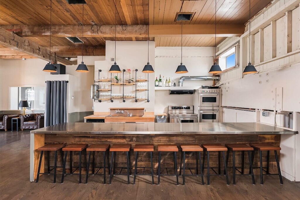 An industrial loft space in Seattle with a huge, 10-person island facing a gourmet kitchen brightly lit by overhead lights and huge windows