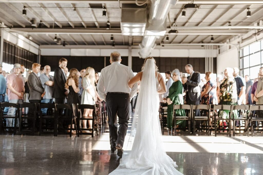 A father escorts his daughter down an aisle at an industrial wedding venue